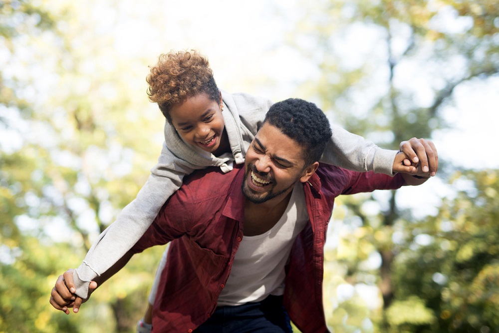 Happy family. Father carrying daughter on his shoulders piggyback and smiling.